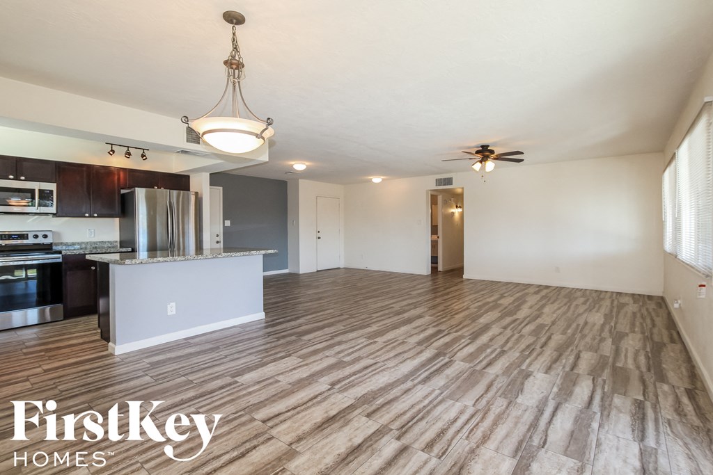 an empty living room with a kitchen and a ceiling fan