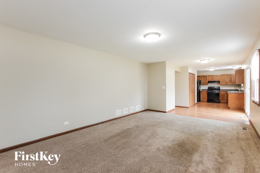A spacious room with a carpeted floor and a kitchen area in the background.