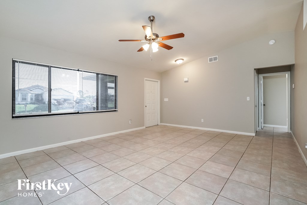 an empty living room with a large window and a ceiling fan