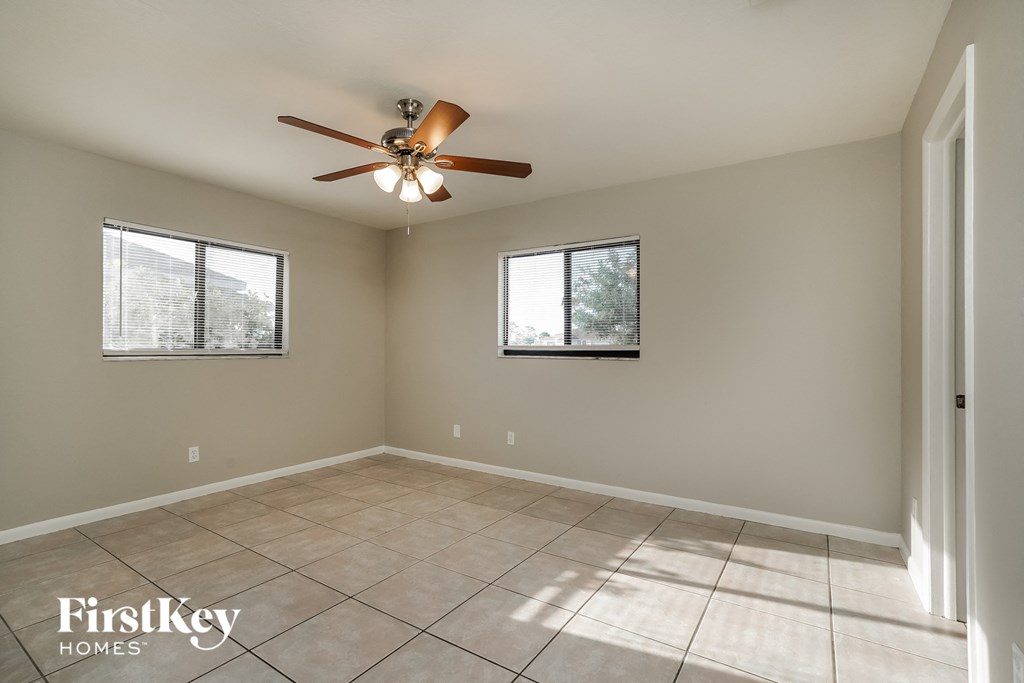 an empty room with a ceiling fan and two windows
