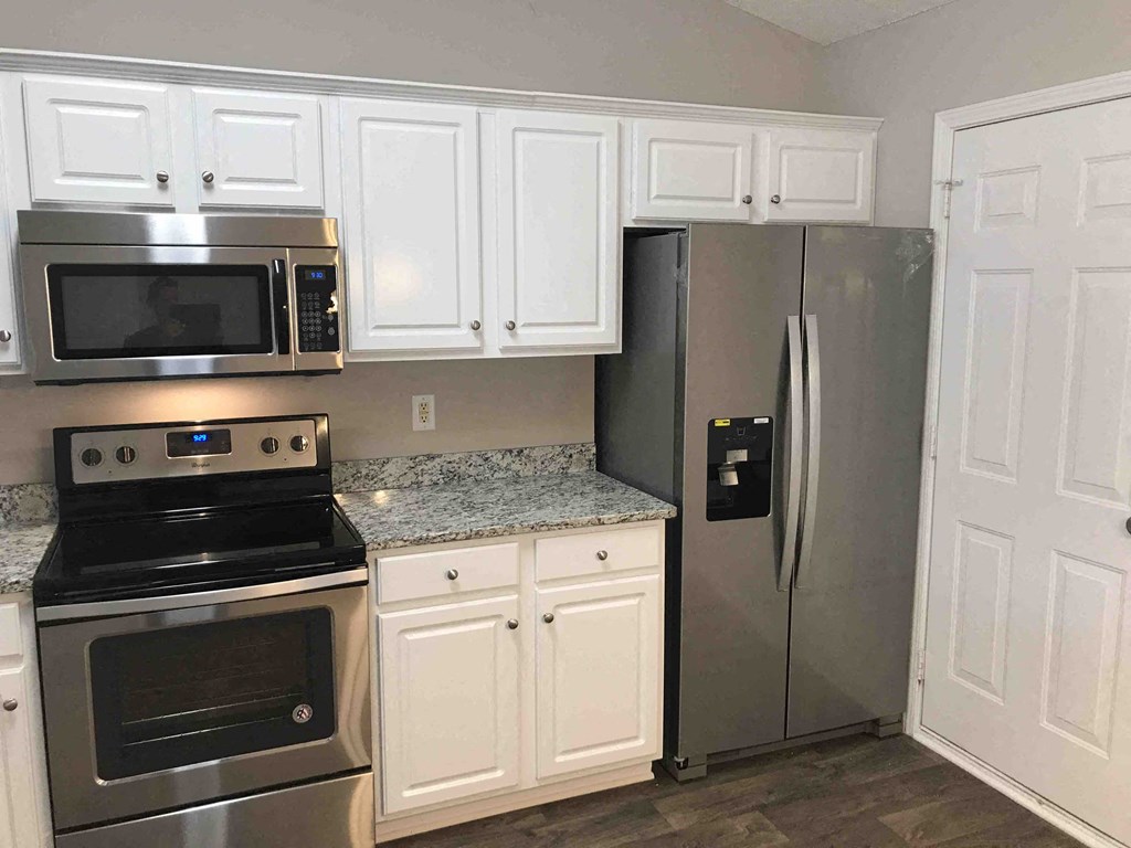 A kitchen with a stove, microwave, refrigerator, and cabinets.