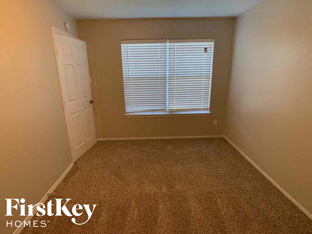 A room with a carpeted floor, a window with blinds, and a door.