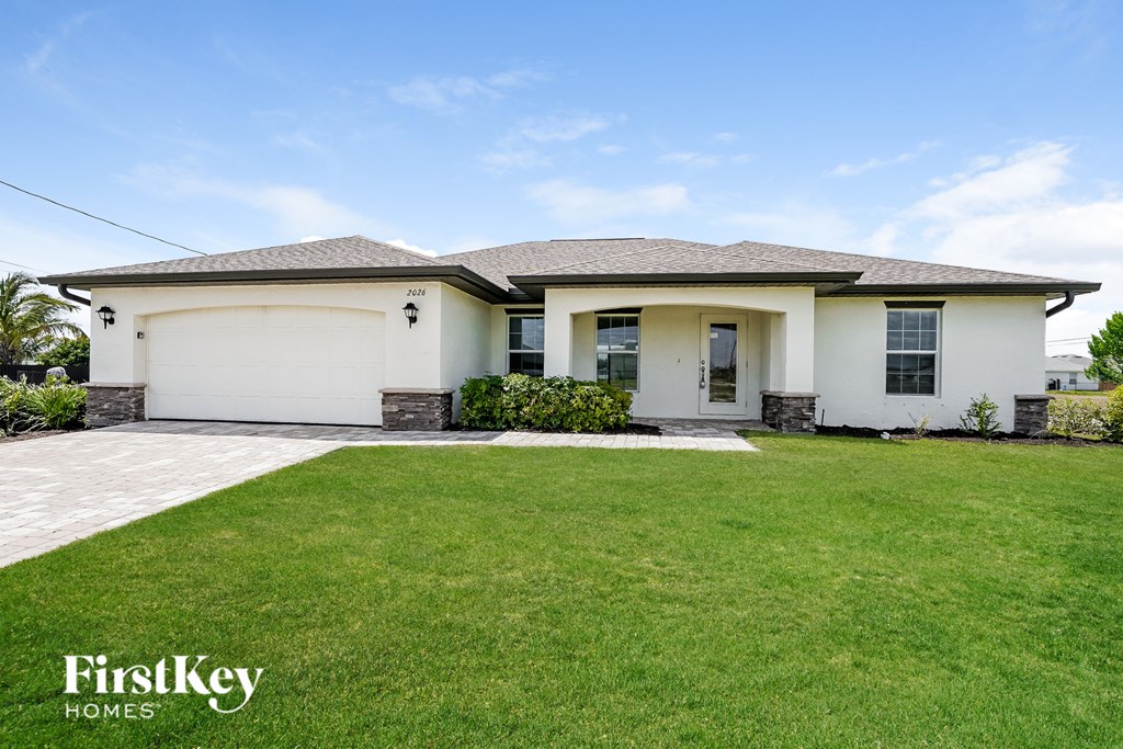 A white house with a grey roof and a green lawn in front.