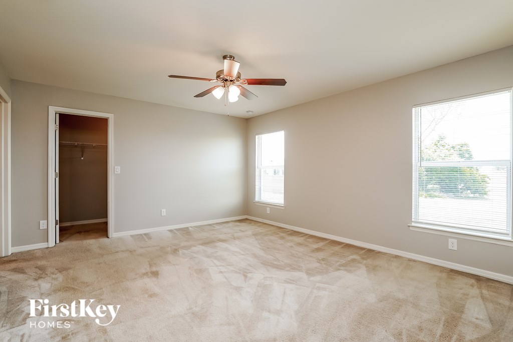A spacious room with a ceiling fan and two windows.