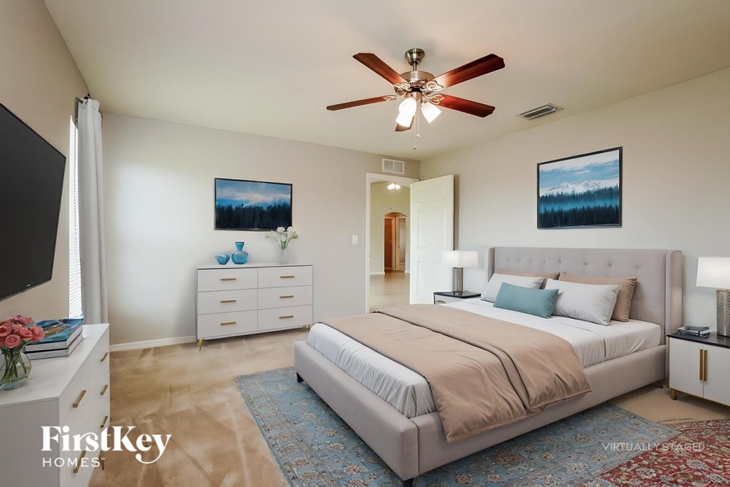 A bedroom with a large bed, a ceiling fan, and two framed pictures on the wall.