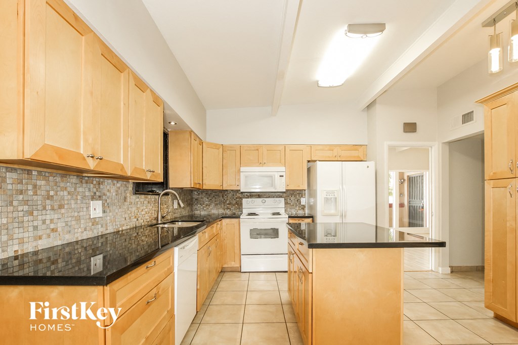 a kitchen with black counter tops and wooden cabinets and a white refrigerator