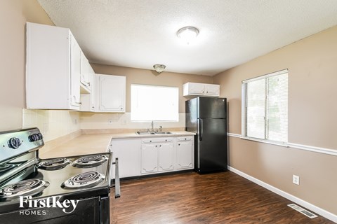 A kitchen with a black refrigerator, white cabinets, and a stove top oven.