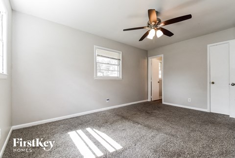 A spacious room with a ceiling fan and two windows.