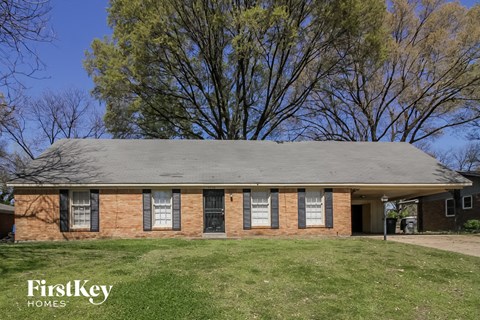 the front of a brick house with a green lawn and some trees