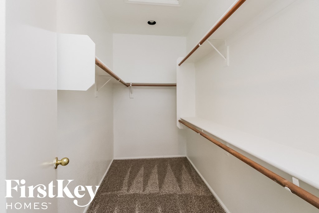 a walk in closet in a bathroom with white walls and a wooden railing