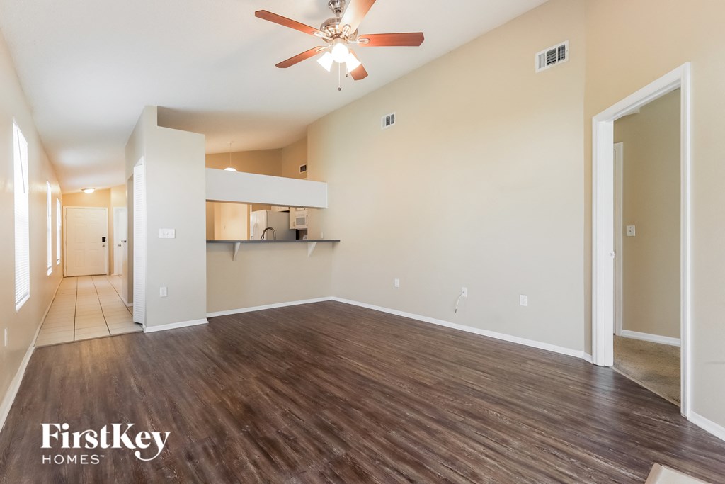 an empty living room with a ceiling fan and a kitchen