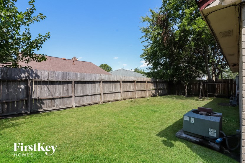 a backyard with a wooden fence and a grill in the grass