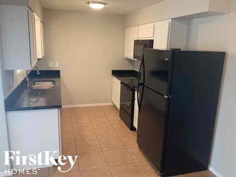 A black fridge in a kitchen with white cabinets and a black counter.