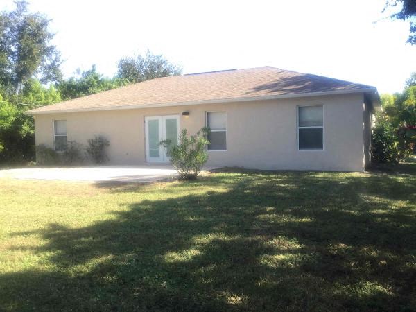 A house with a brown roof and white walls with a green lawn in front.