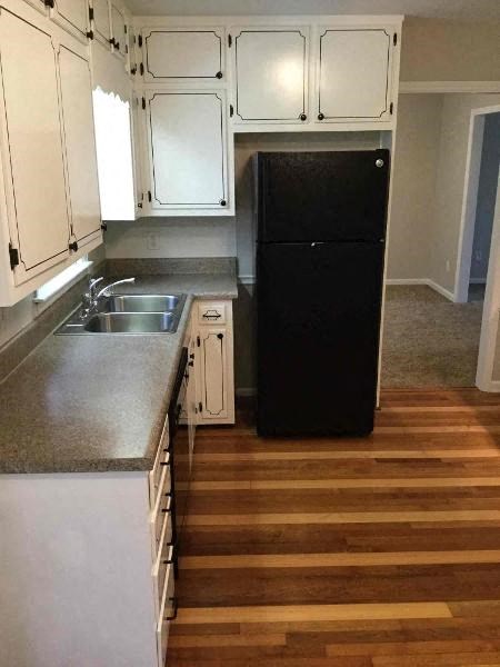 A black refrigerator in a kitchen with white cabinets.