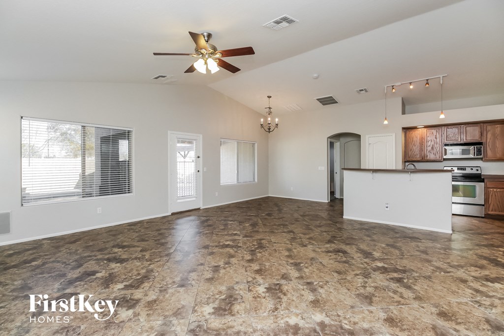 an empty living room with a ceiling fan and a kitchen
