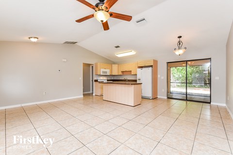 A spacious room with a ceiling fan and a kitchen area in the background.