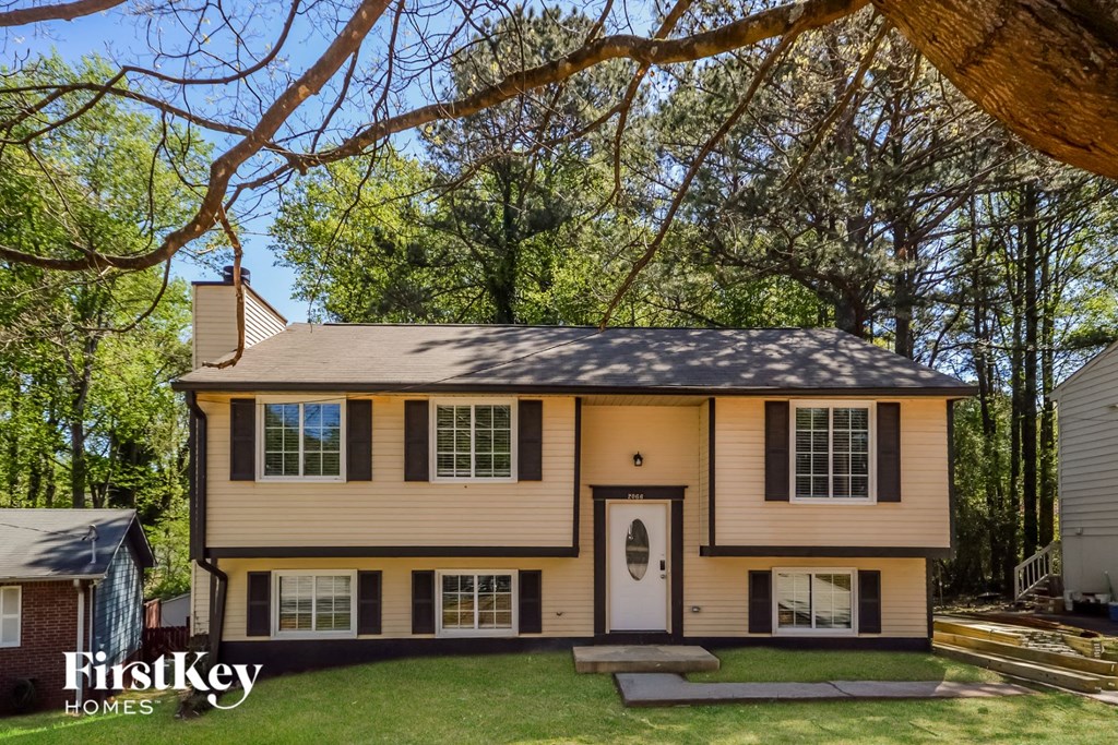 a yellow house with black shutters and a yard with trees