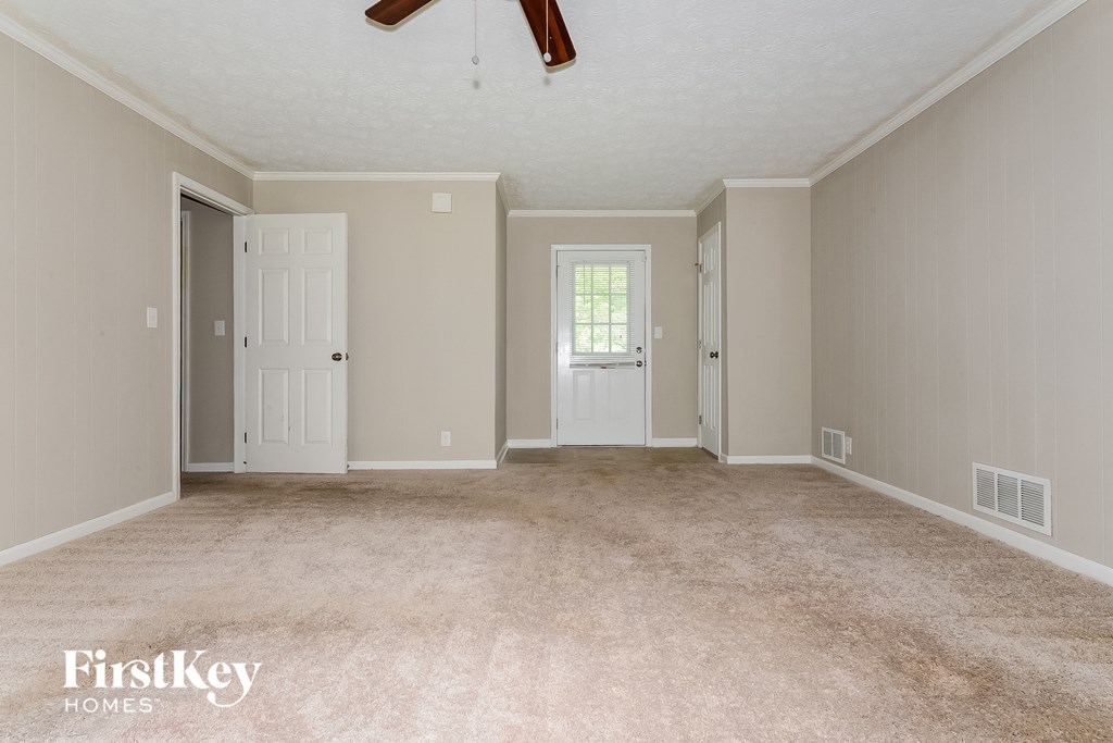 a carpeted living room with two doors and a ceiling fan