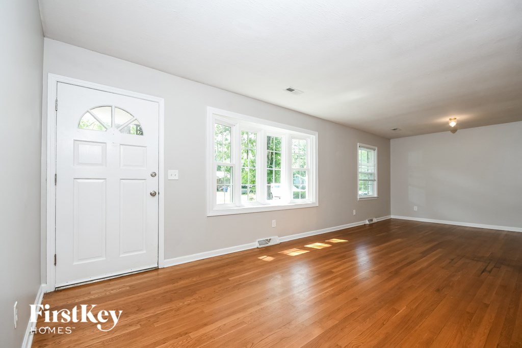 A room with wooden floors and white walls, with a door and a window.