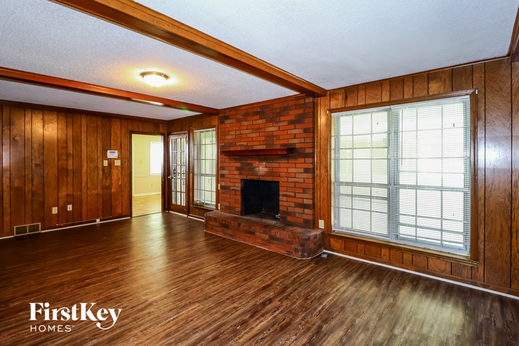 an empty living room with a brick fireplace and wooden floors