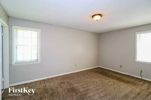 the living room of a house with carpet and two windows