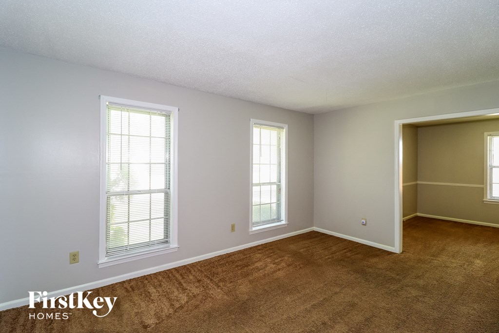 a living room with a brown carpet and two windows