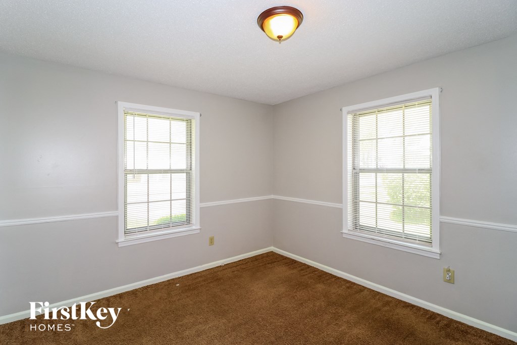 a bedroom with a brown carpet and two windows