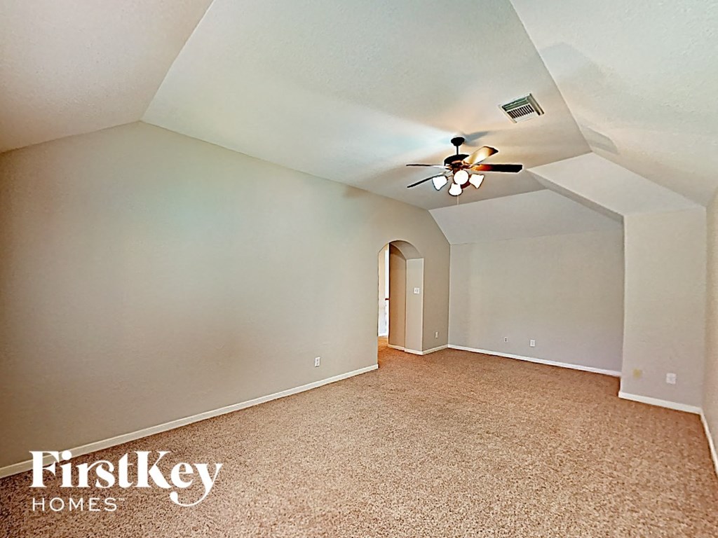 A spacious room with a ceiling fan and a doorway leading to another room.