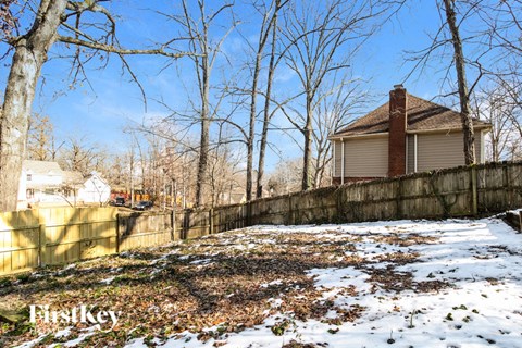 A house with a brown roof is surrounded by a fence and leafless trees.