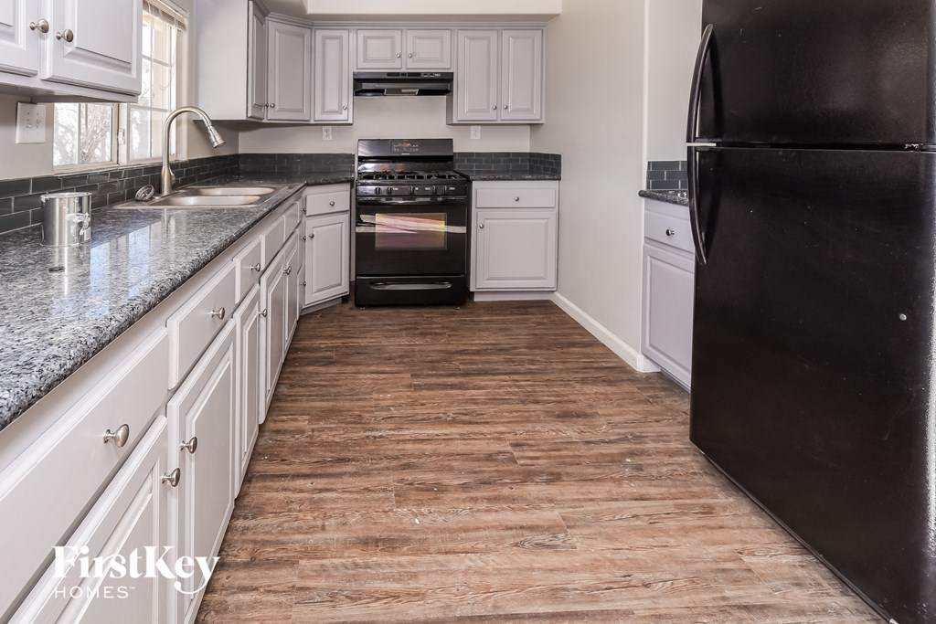 a kitchen with white cabinets and black appliances and a wood floor