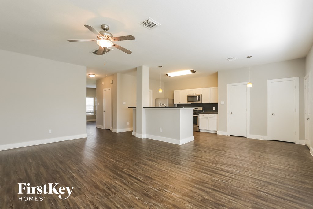 an empty living room with a ceiling fan and a kitchen