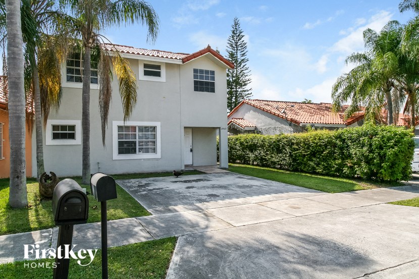 a white house with a driveway and palm trees