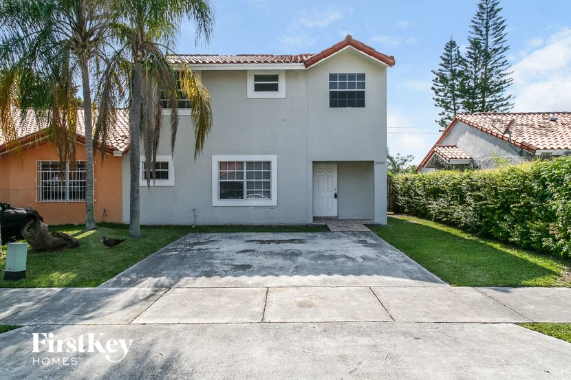 a white house with a driveway and palm trees
