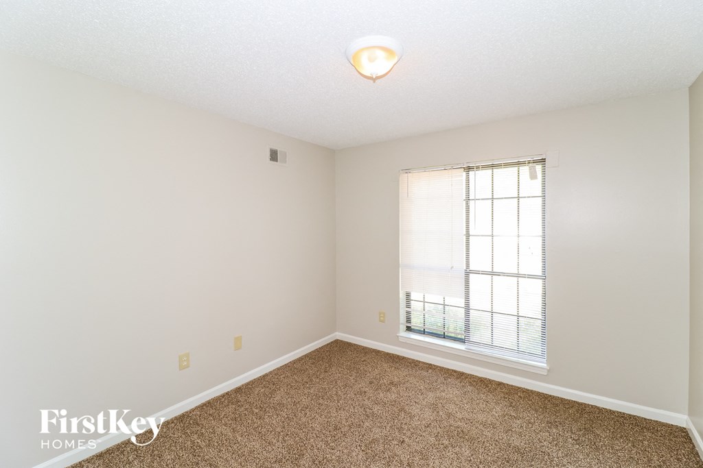 a spacious bedroom with a large window and carpeted flooring