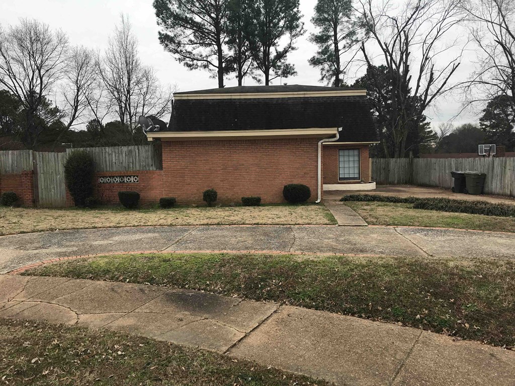 A small house with a brick exterior and a black roof sits in a yard with a fence.