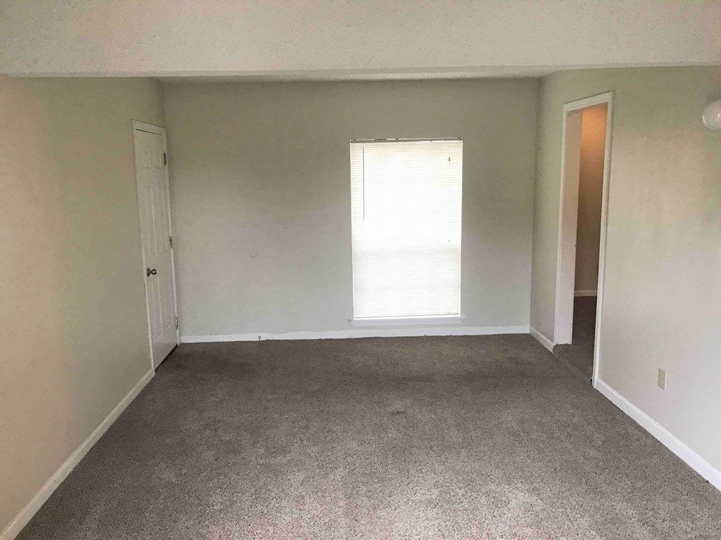 A room with a carpeted floor and a window letting in sunlight.