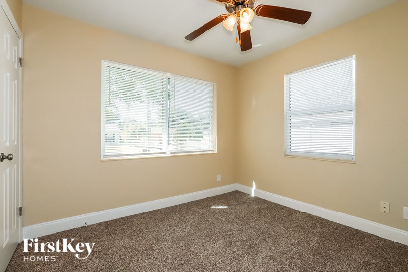 an empty bedroom with a ceiling fan and two windows
