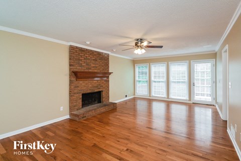 an empty living room with a brick fireplace and a ceiling fan