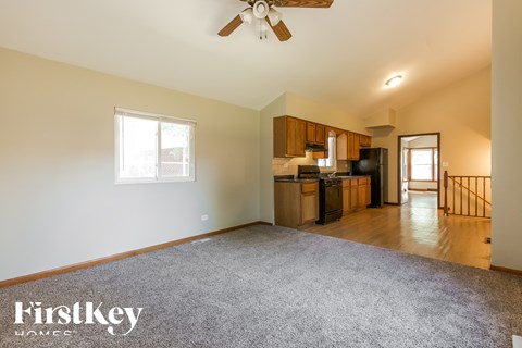 A spacious living room with a kitchen in the background and a carpet on the floor.