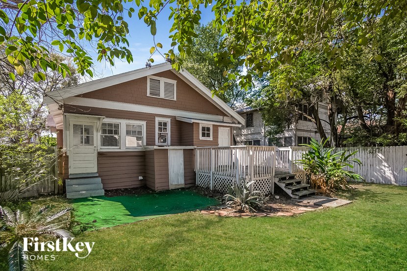 a small brown house with a yard and a white fence