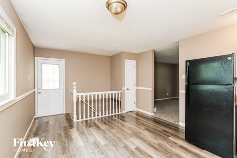 A kitchen area with a black fridge and wooden flooring.