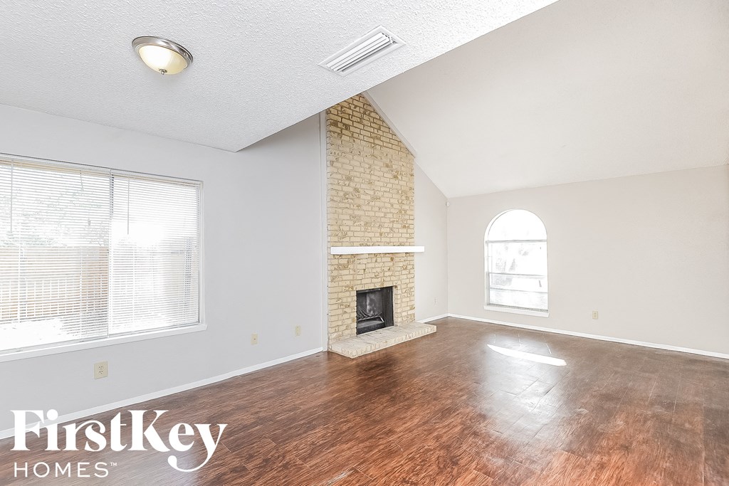 an empty living room with a brick fireplace and wood floors
