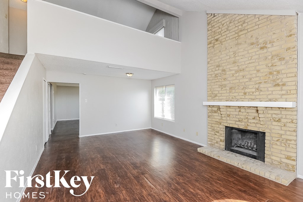 an empty living room with a brick fireplace and wood floors