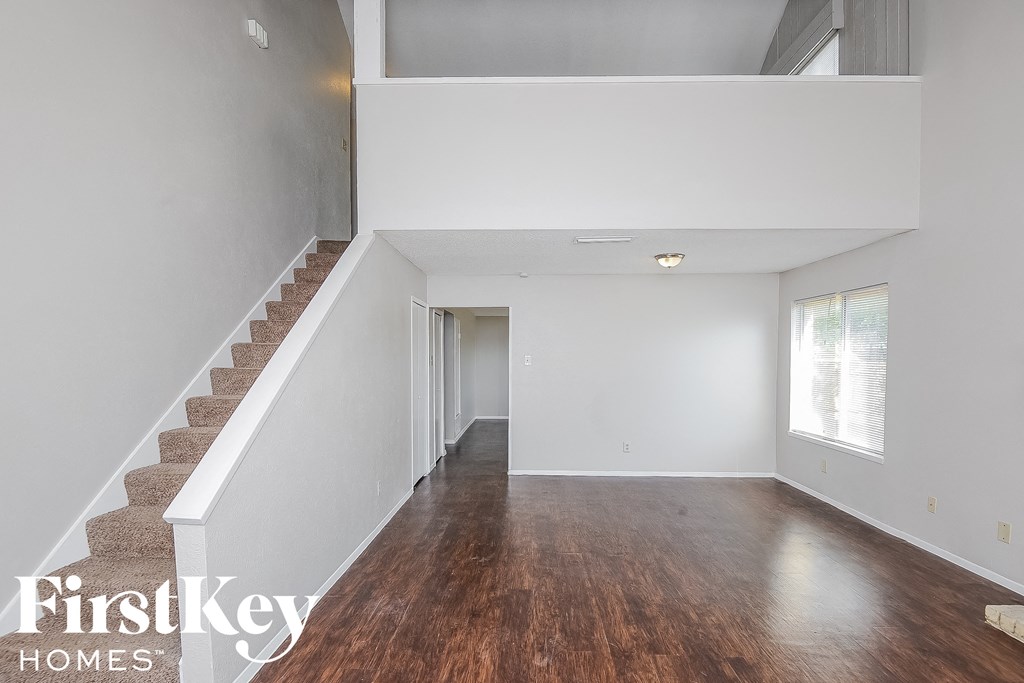 a living room with a staircase and white walls and wood floors