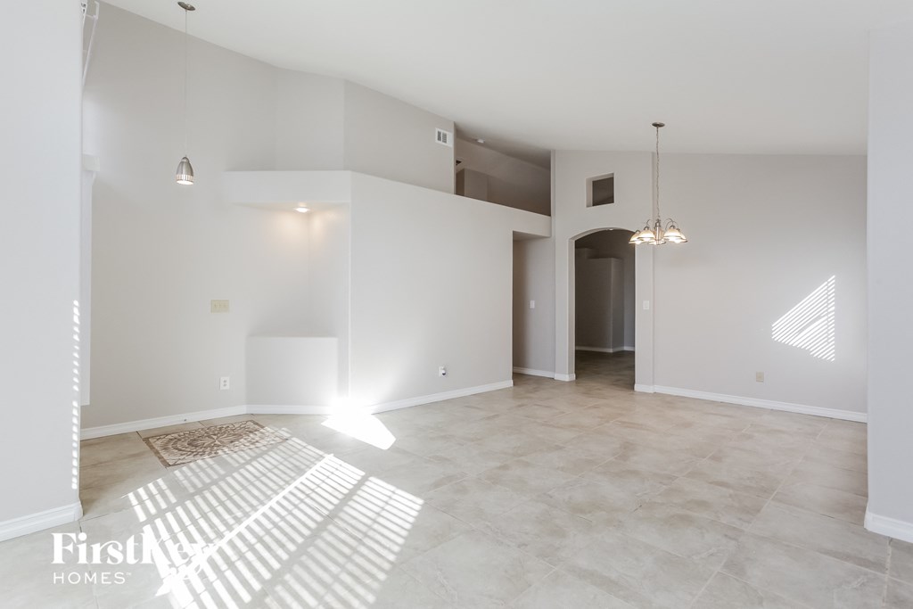 A spacious, empty room with a rug on the floor and a chandelier hanging from the ceiling.