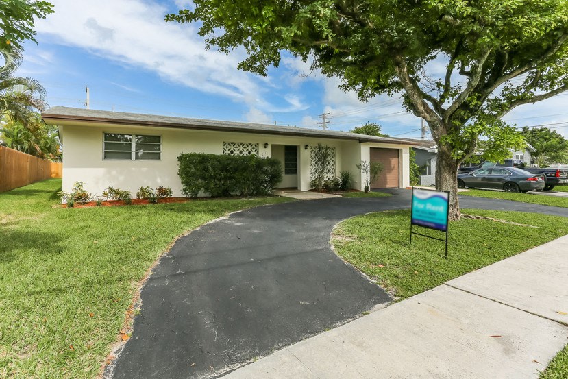 a white house with a driveway and a blue sign in the grass