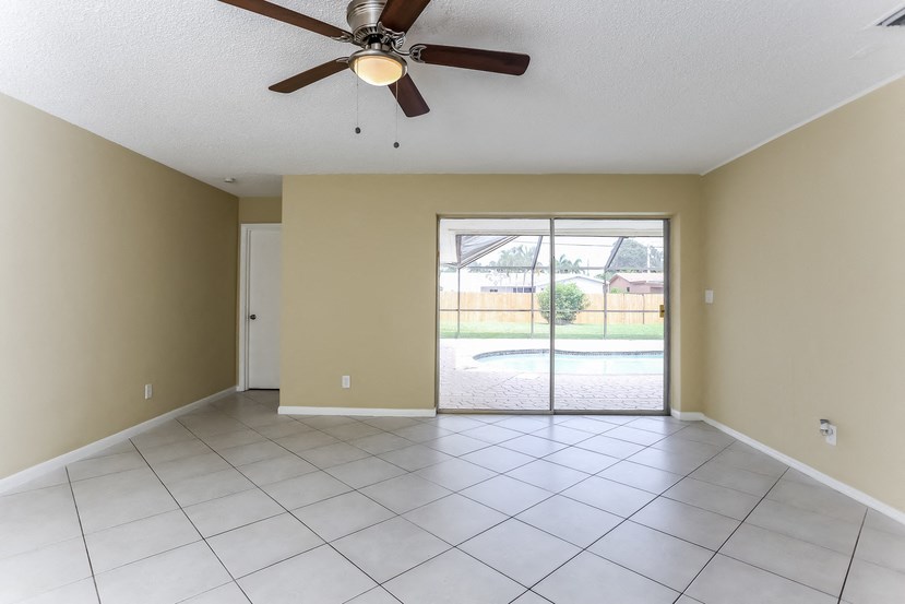 an empty living room with a ceiling fan and a door to a pool