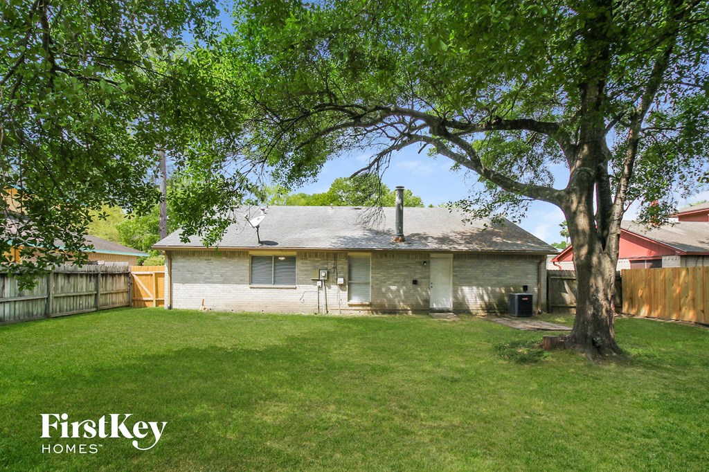a backyard with a white brick house and a tree