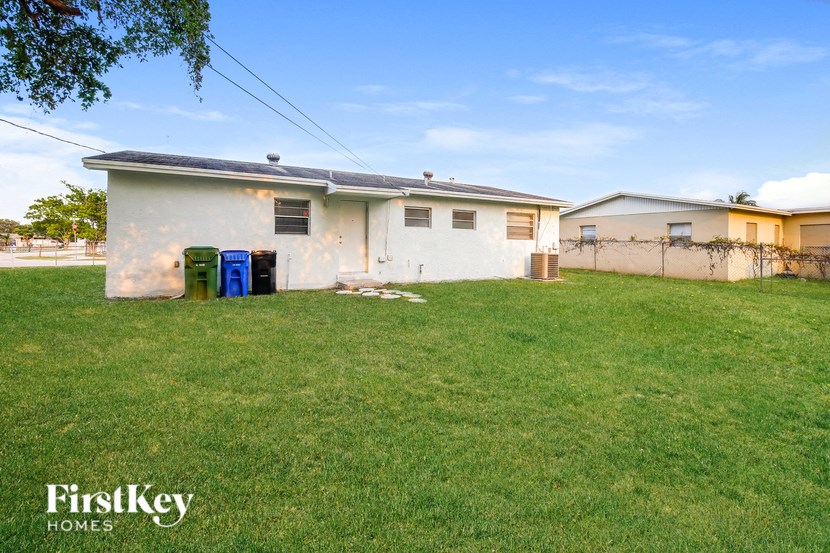 A white house with a blue and green dumpster in front of it.